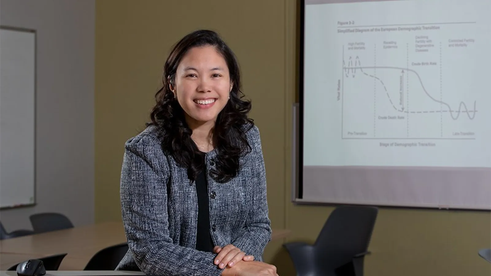 A woman with dark hair and a suit sitting in a conference room.
