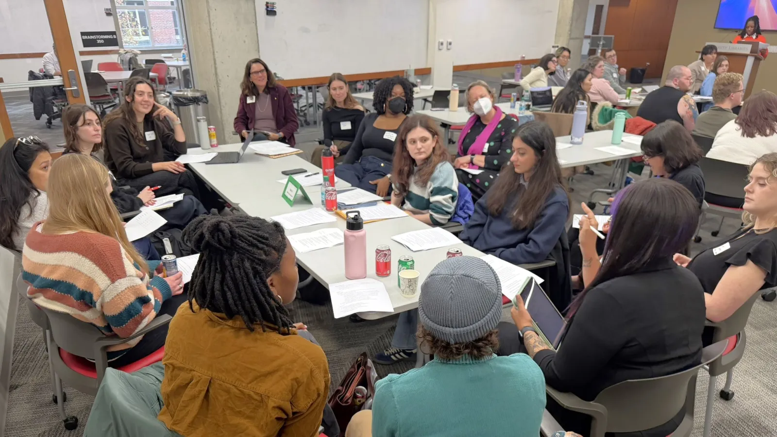 Diverse group of graduate students sitting around a table listening to a student speaking.