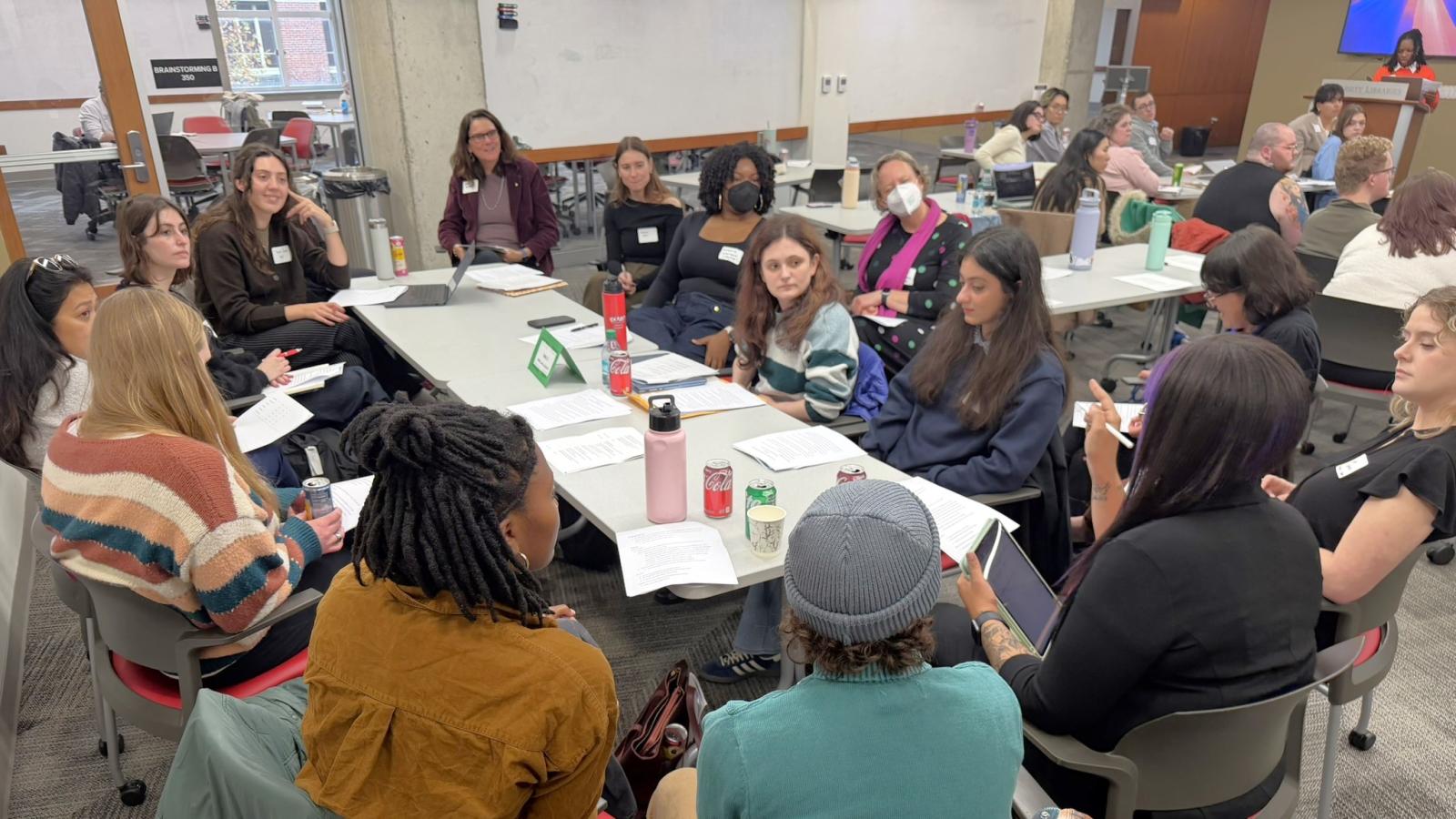 Diverse group of graduate students sitting around a table listening to a student speaking.