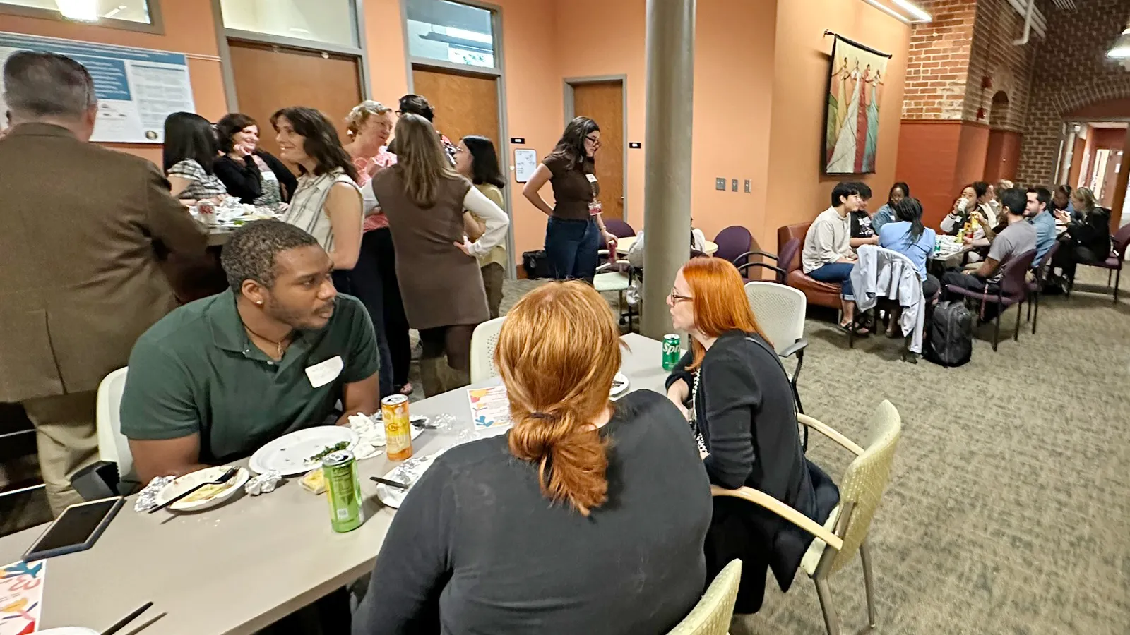 Groups of students and faculty in open office space having conversations while standing and sitting