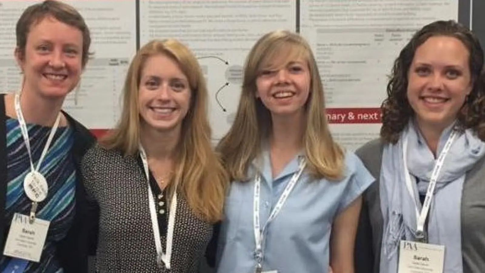 Image of Sarah Hayford, Karen Guzzo, Vanessa Lang, and Sarah Garver standing in front of the poster.