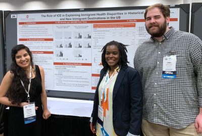 Three graduate students stand by their poster presentation at a PAA conference