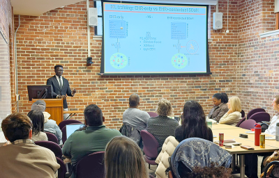 Speaker presenting his research with PowerPoint slides to a group of faculty, research staff, and students.