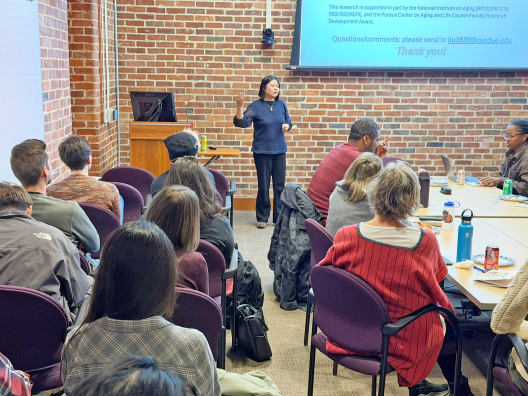 Professor presenting her research, standing in front of room full of faculty and students..