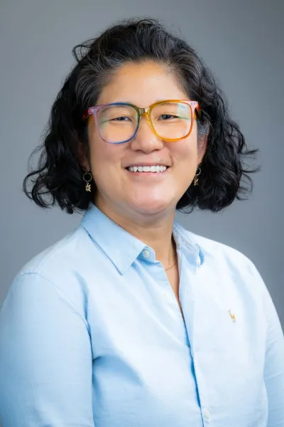 Asian woman with glasses, short black hair and a blue dress shirt.