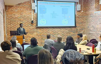 Speaker presenting his research with PowerPoint slides to a group of faculty, research staff, and students.