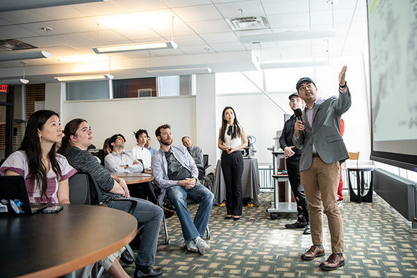Student speaking and pointing to projection screen while standing in front group of other students