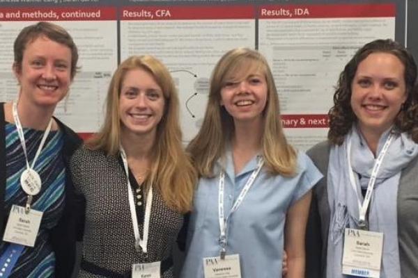 Image of Sarah Hayford, Karen Guzzo, Vanessa Lang, and Sarah Garver standing in front of the poster.