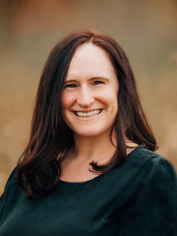 A woman with dark brown hair and a green sweater smiling.